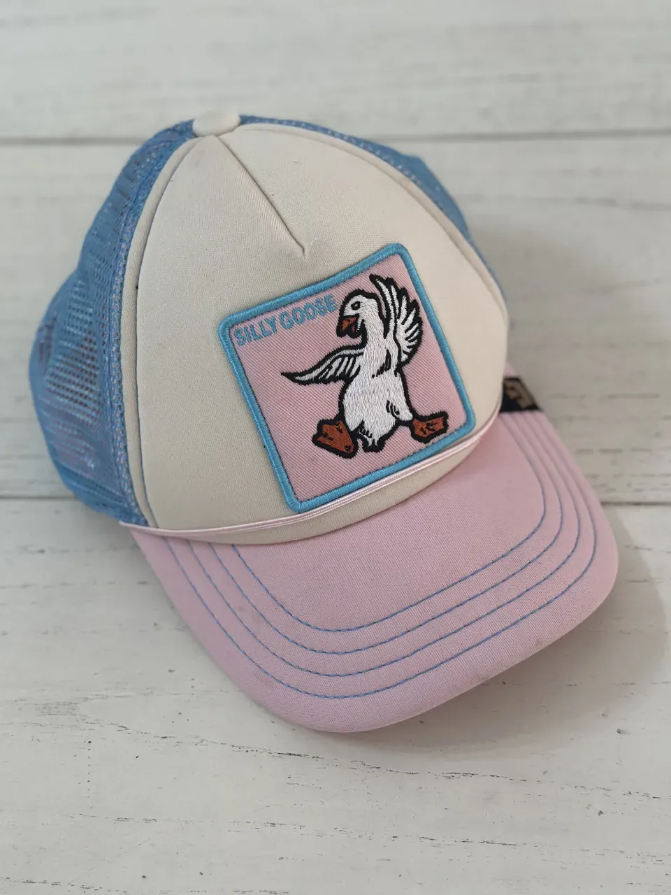 Gorra trucker con frente de espuma blanca, red celeste atrás, visera rosa y un parche bordado con un ganso